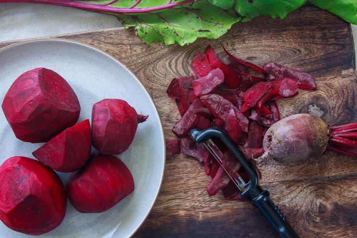 Peeled beets and the peelings on a cutting board showing the process of preparing beets to roast