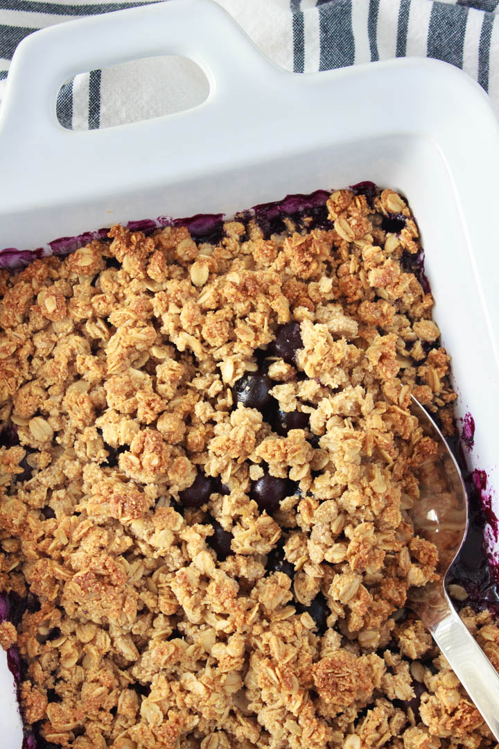 Blueberry crisp done baking, digging a spoon in to serve