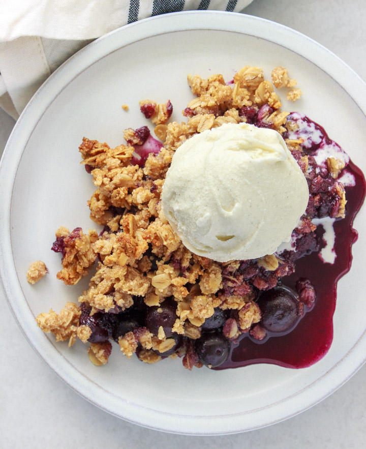Blueberry crisp on a plate with a scoop of vanilla ice cream