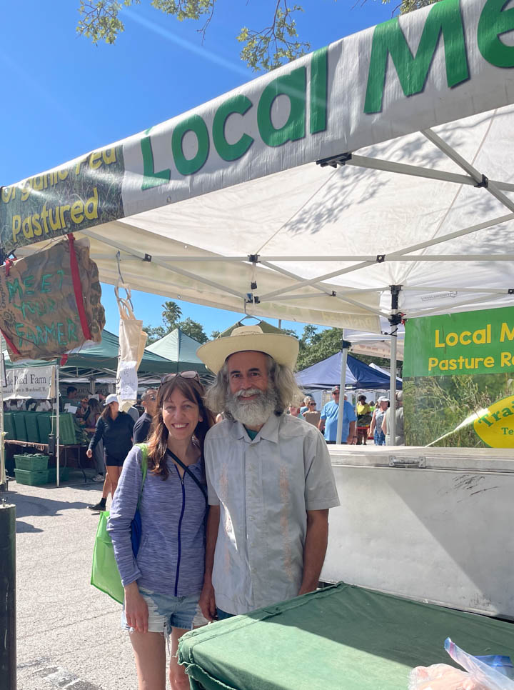 Sara and Travis posing in front of the TrailBale Farm booth at the Saturday Morning Market in St. Petersburg, FL