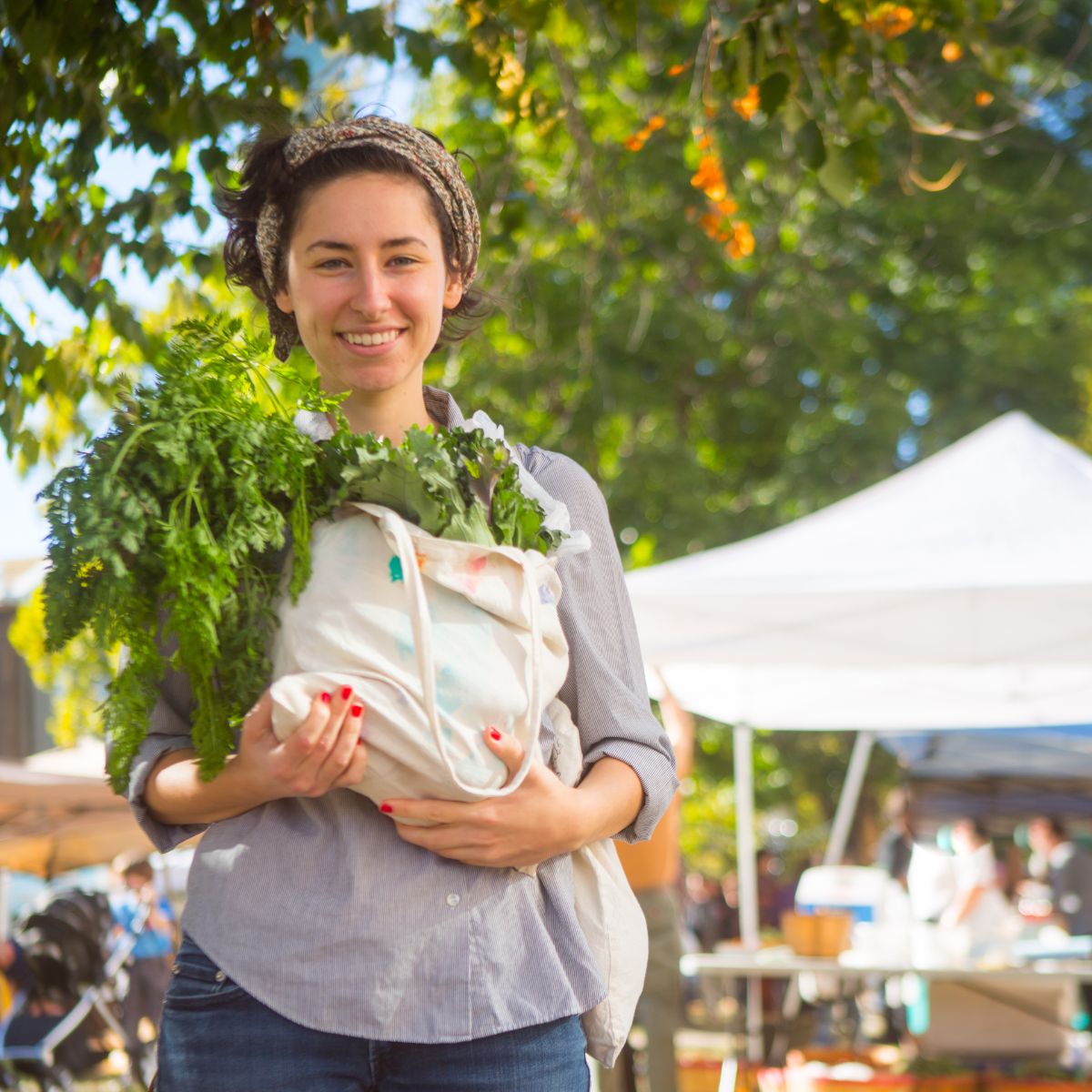 How to Save Money at the Farmers Market (Insider Tips) - Young woman holding a shopping bag of farmers market food